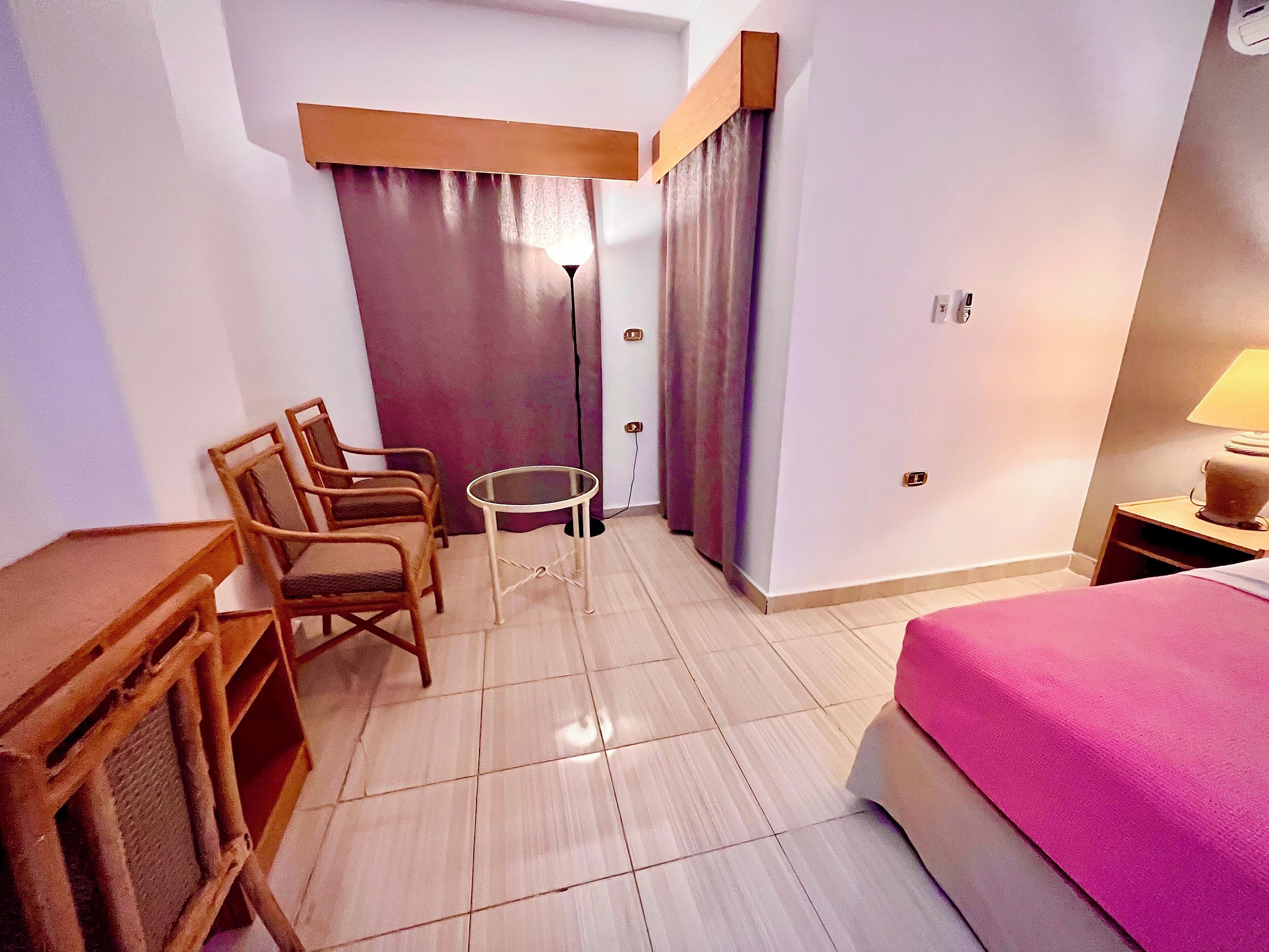 A hotel room with a bed, a desk, two chairs, a small table, and a lamp.