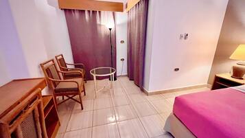 A hotel room with a bed, a desk, two chairs, a small table, and a lamp.