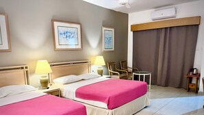 A hotel room with two beds, a small table, two chairs, and an air conditioning unit. - Masaya Suites (Hurghada)