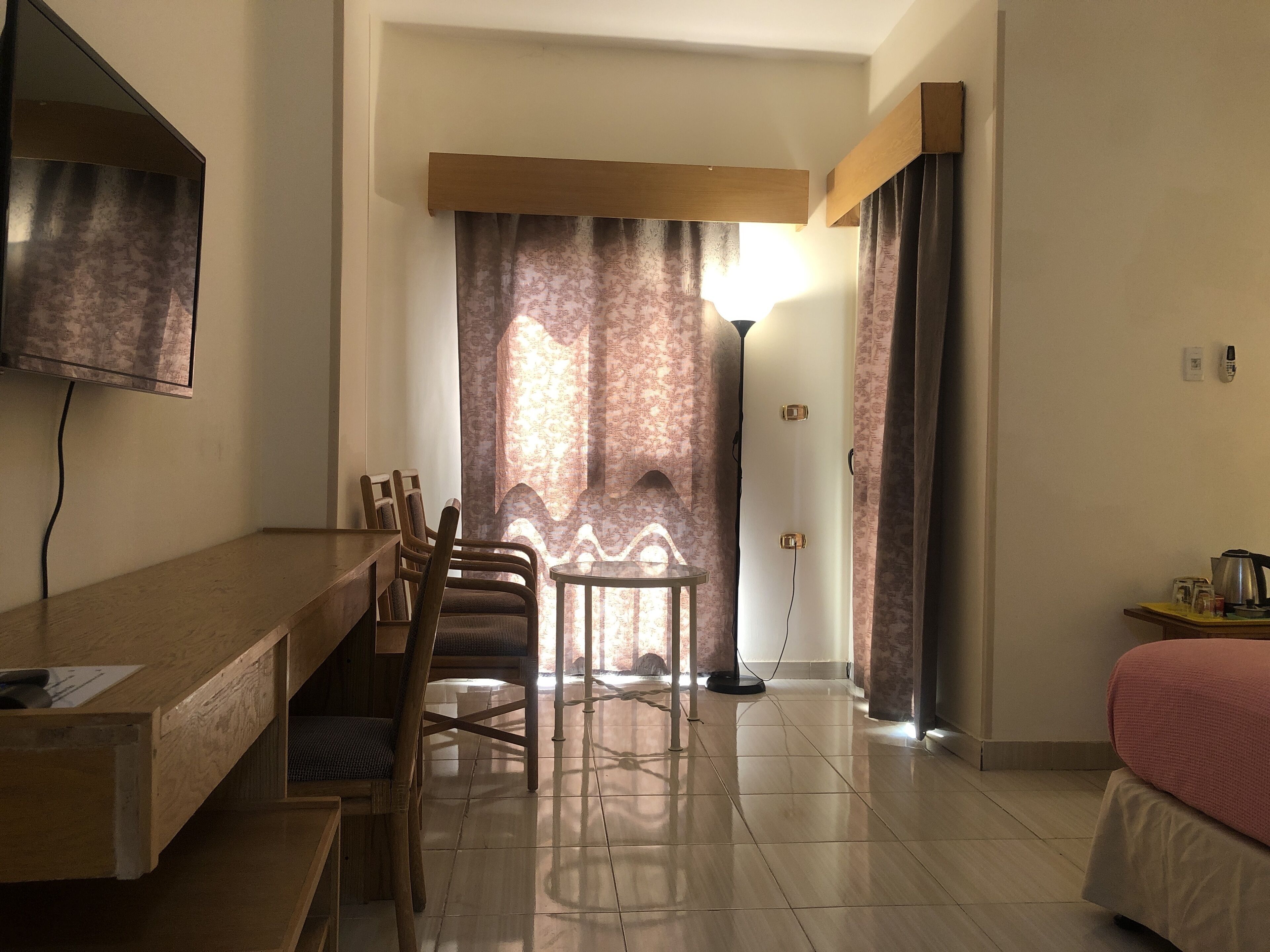 Habitació d'hotel amb escriptori de fusta, cadires, un llit, televisió i una làmpada.