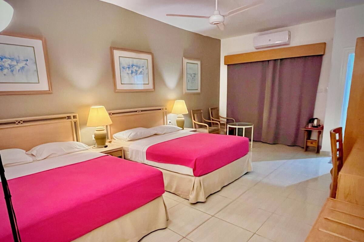 A hotel room with two beds, a ceiling fan, a small table, and a chair.