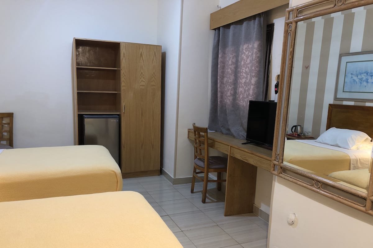 A hotel room with two beds, a wooden desk with a computer, a wardrobe, and a mirror.