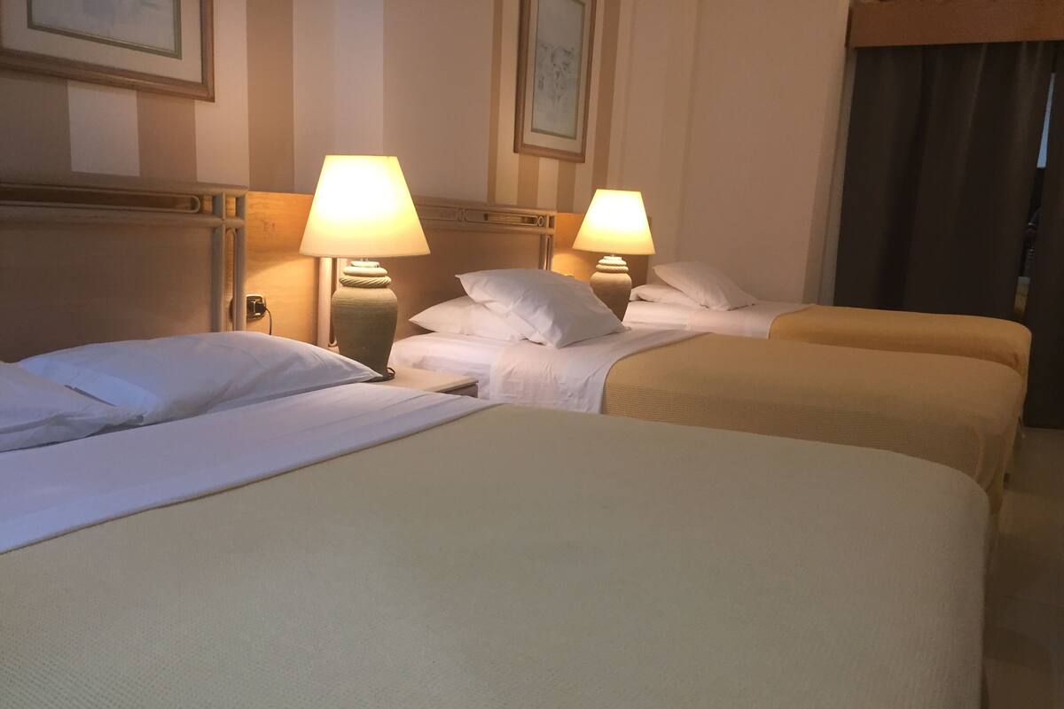 A hotel room with two beds, each with white linens and pillows, and two bedside lamps.