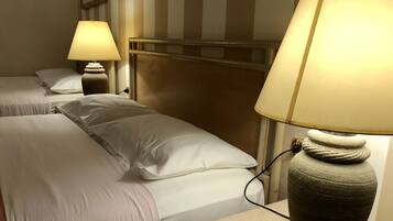 A hotel room with two beds, each with white linens and pillows, a headboard, and a bedside lamp with a textured base.