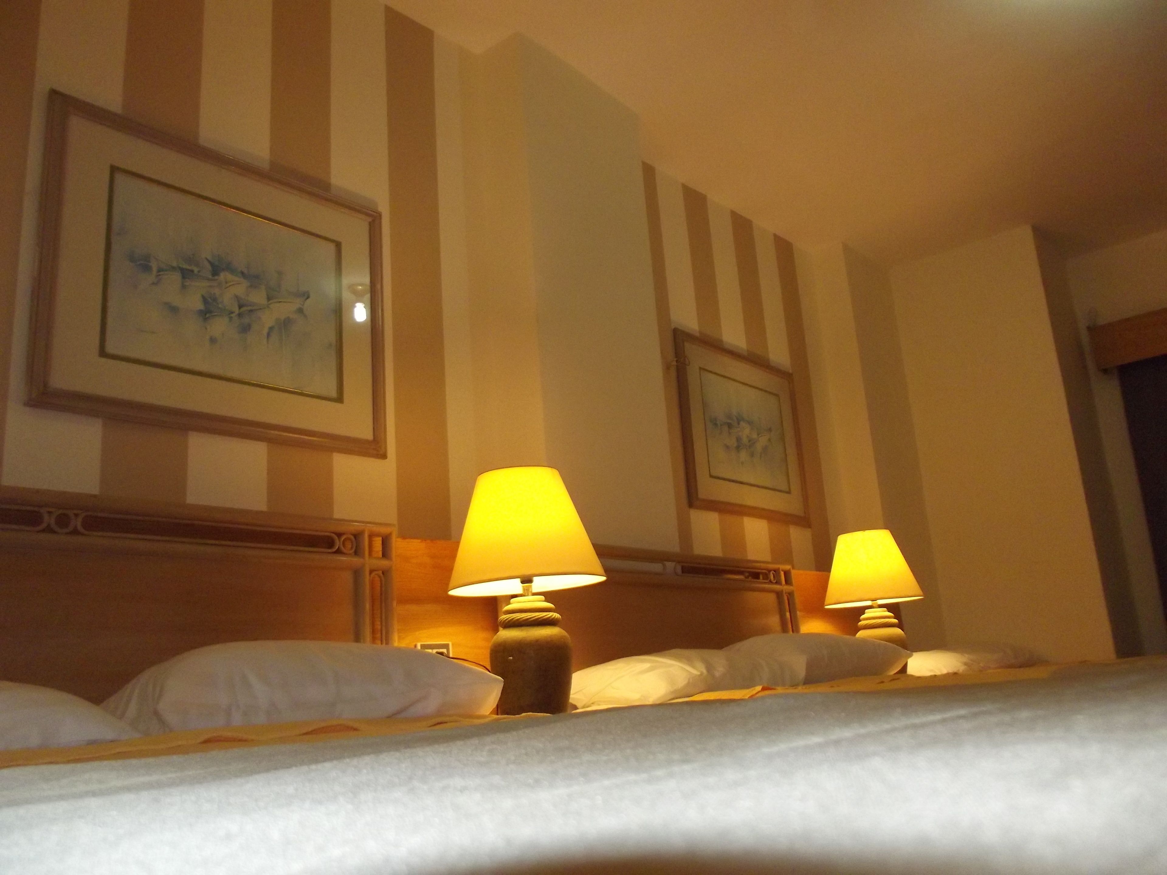 Habitación de hotel con paredes a rayas, dos lámparas de noche y dos cuadros enmarcados sobre la cama.