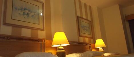 Habitación de hotel con paredes a rayas, dos lámparas de noche y dos cuadros enmarcados sobre la cama.