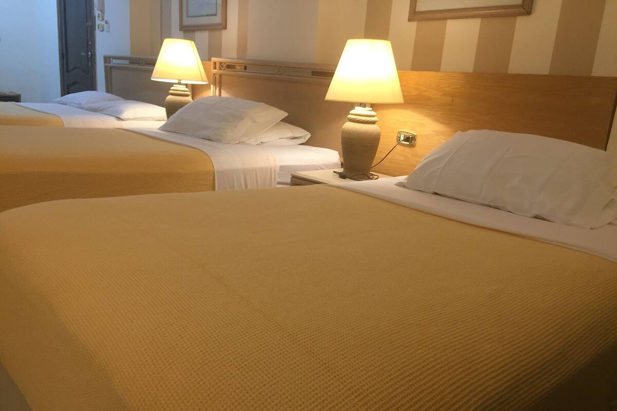 A hotel room with two beds, each with a headboard and a bedside lamp.