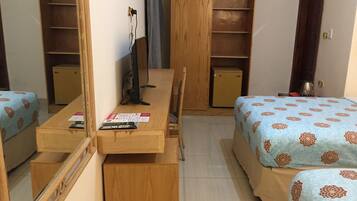 Habitación de hotel compacta con dos camas individuales, un escritorio de madera con silla, un armario pequeño y un espejo.