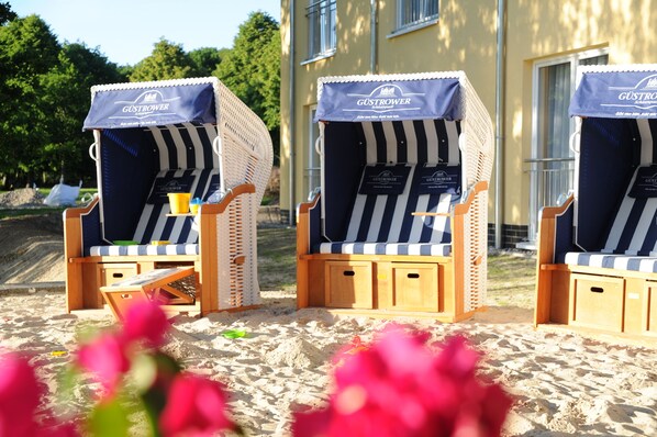 Three beach chairs with striped cushions and a blue canopy, each with a small table and a yellow cup.
