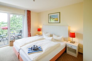 A hotel room with a large bed, two bedside tables with lamps, a window with a view of the outdoors, and a painting on the wall. - Strandhaus am Inselsee (Guestrow)