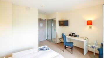 Ein Hotelzimmer mit Bett, Schreibtisch, Stuhl, Fernseher und einem kleinen Tisch mit Lampe.