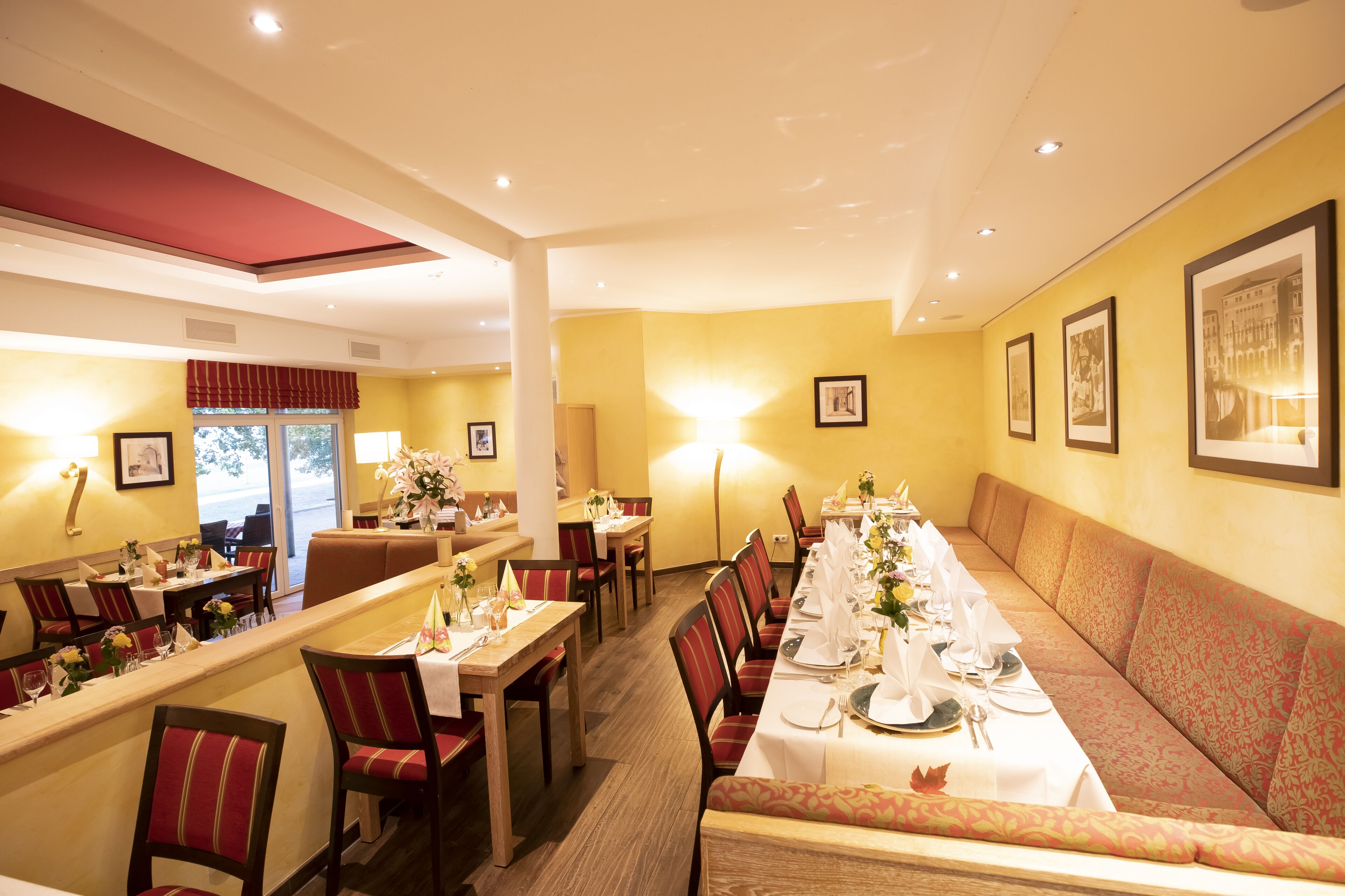 A restaurant with a long dining table set for a meal, surrounded by booths and individual tables.