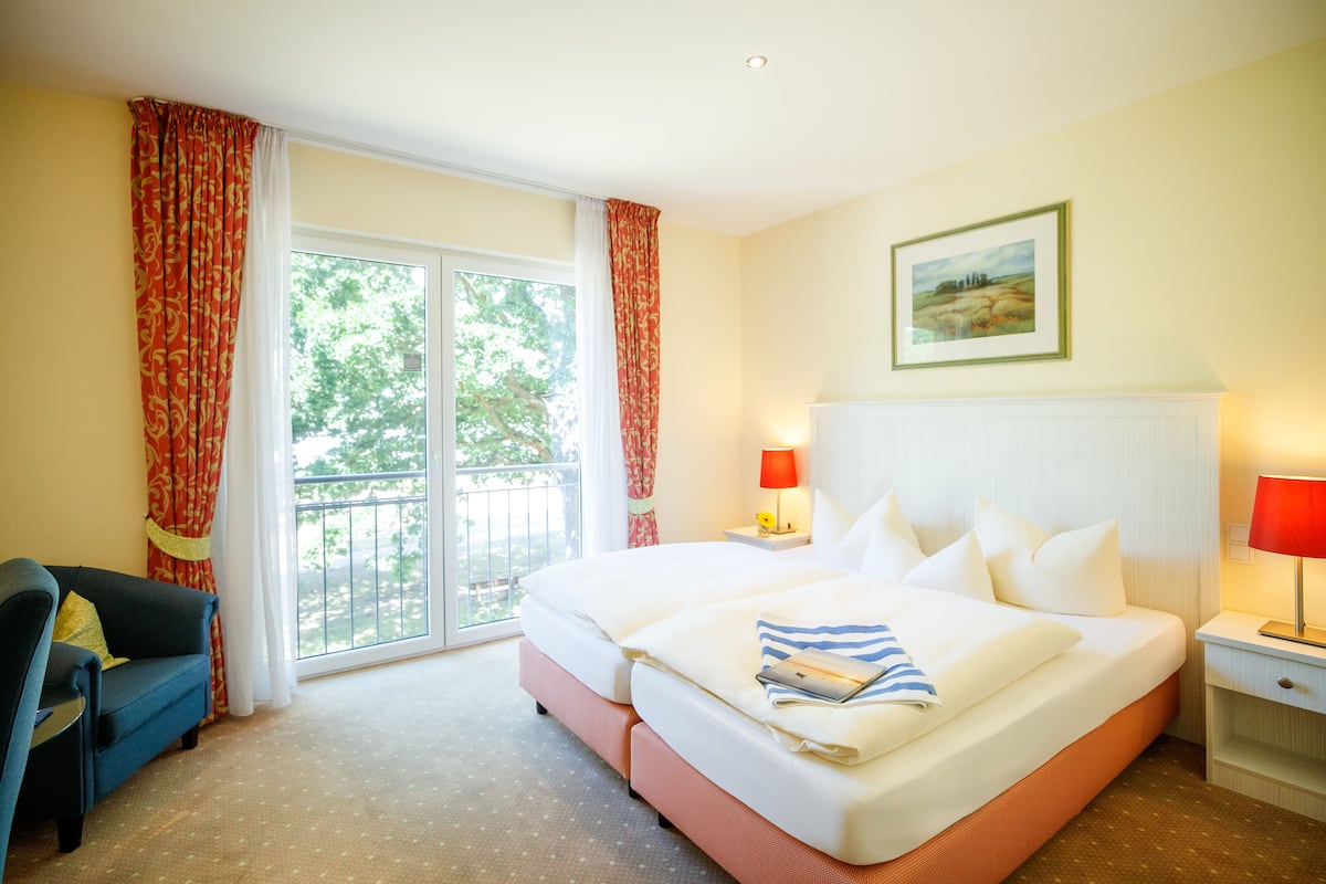 A hotel room with a large bed, a sofa, a desk, and a balcony with curtains.