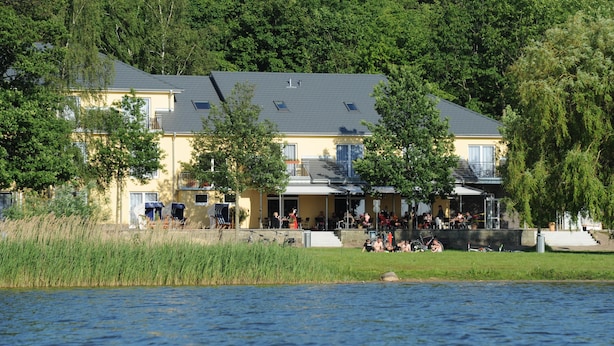 A lakeside building with a balcony, a covered outdoor seating area, and a view of the lake.