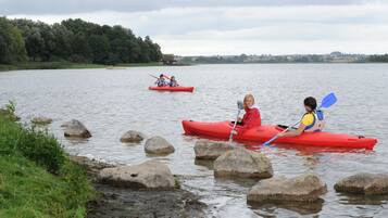 Two people kayaking on a calm lake with large rocks in the foreground and a forested area in the background.