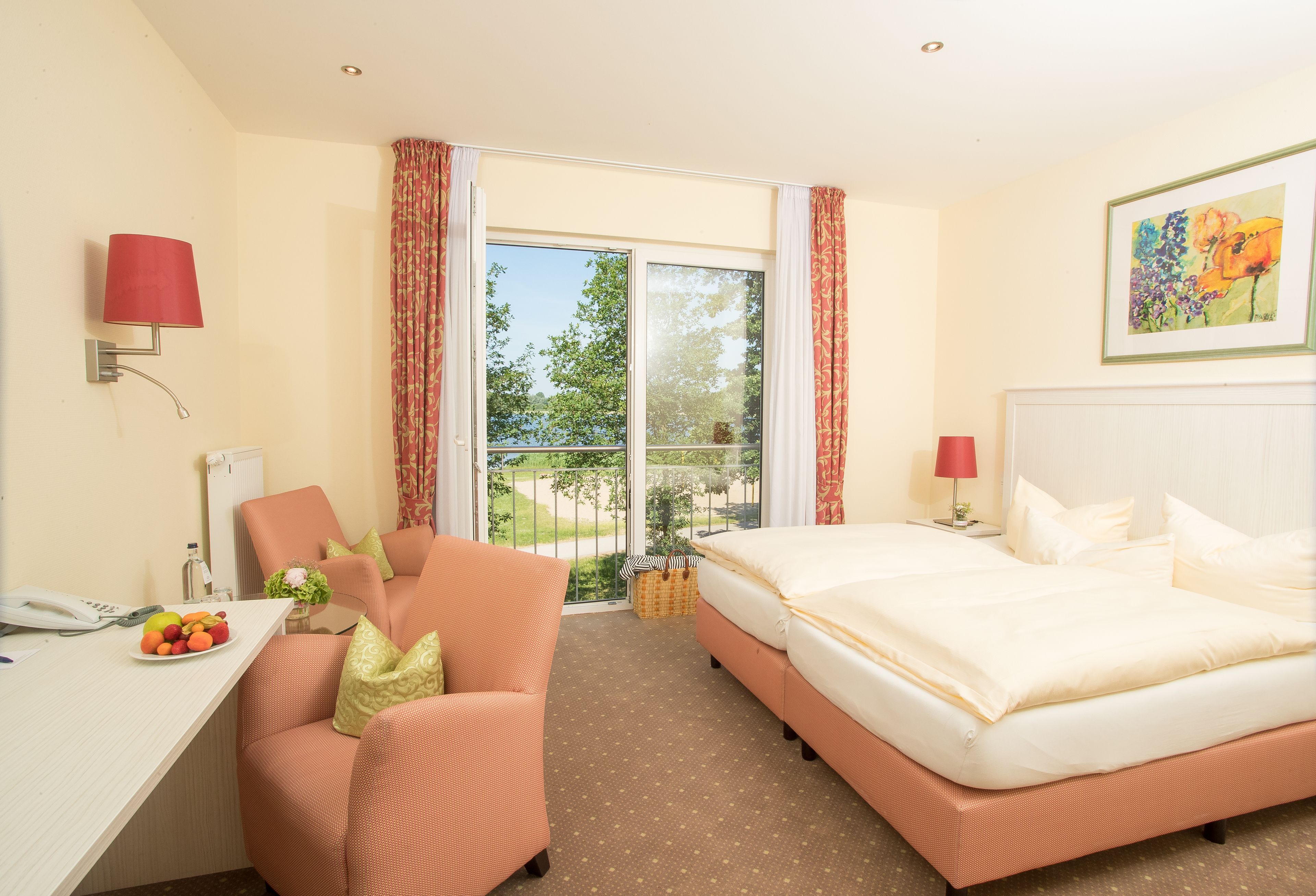 Habitación de hotel con cama, escritorio con teléfono, silla, mesita con fruta y vistas al exterior.