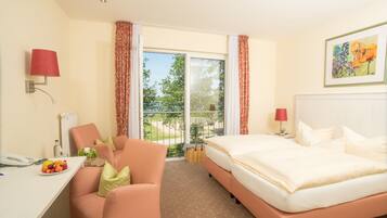 Habitación de hotel con cama, escritorio con teléfono, silla, mesita con fruta y vistas al exterior.