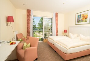 A hotel room with a bed, a desk with a phone, a chair, a small table with fruit, and a view of the outdoors.