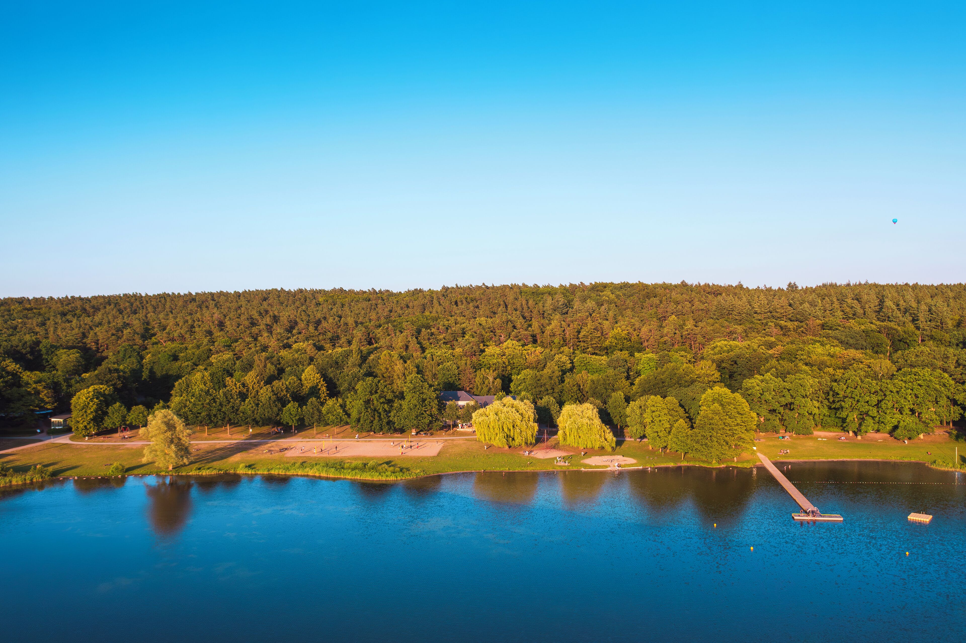 Une vue sur le lac, avec une jetée s’avançant dans l’eau, entourée d’une forêt dense et sous un ciel dégagé.