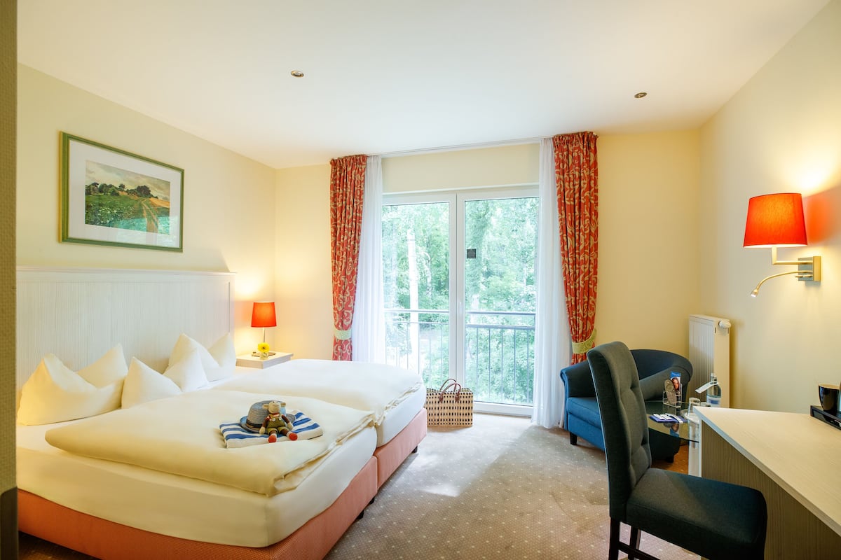 A hotel room with a bed, a desk, a chair, a lamp, and a window with curtains.