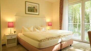 A hotel room with a large bed, two bedside lamps, a framed picture on the wall, and a window with a view of trees.