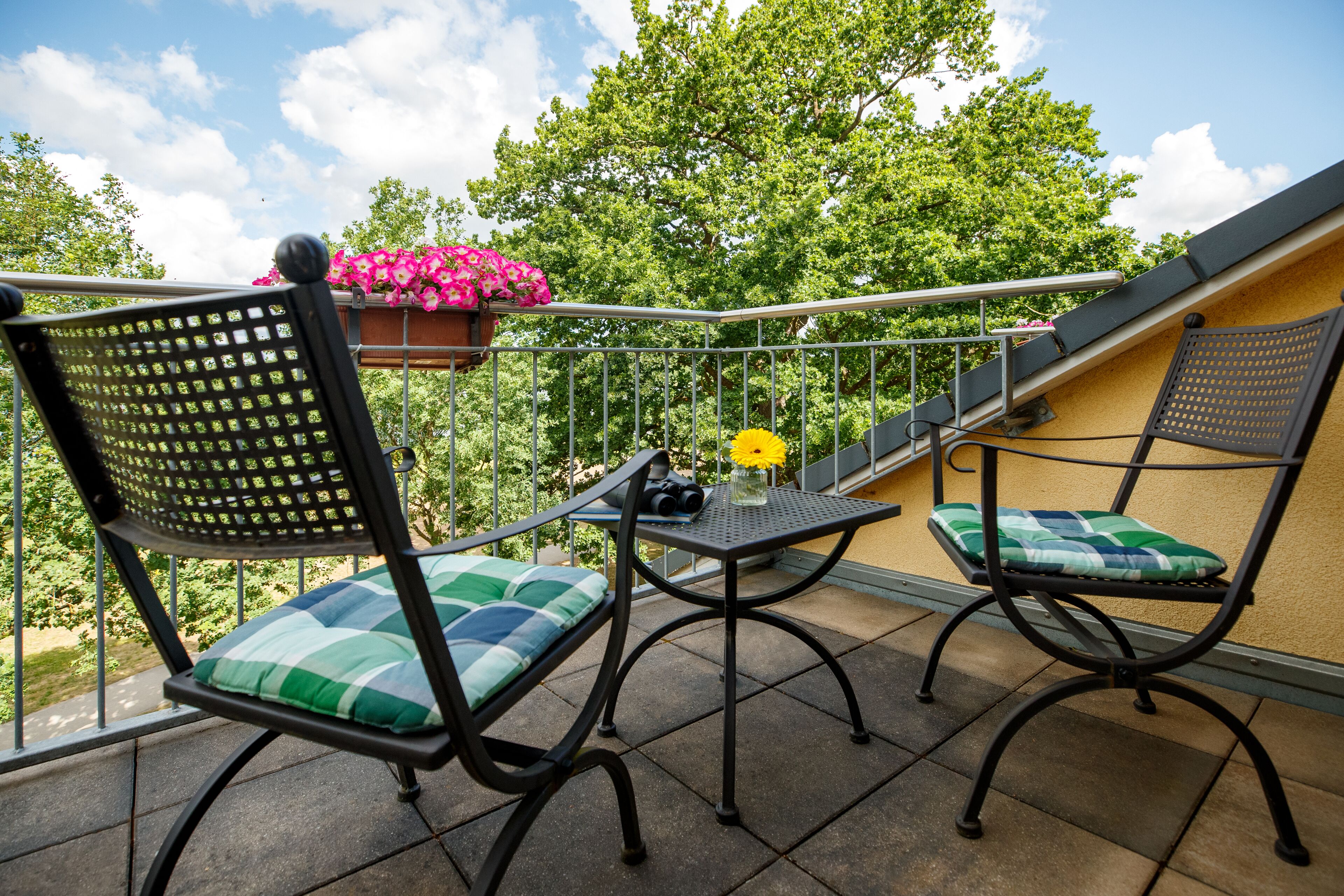 Een balkon met twee stoelen, een tafel en een bloemenmand.