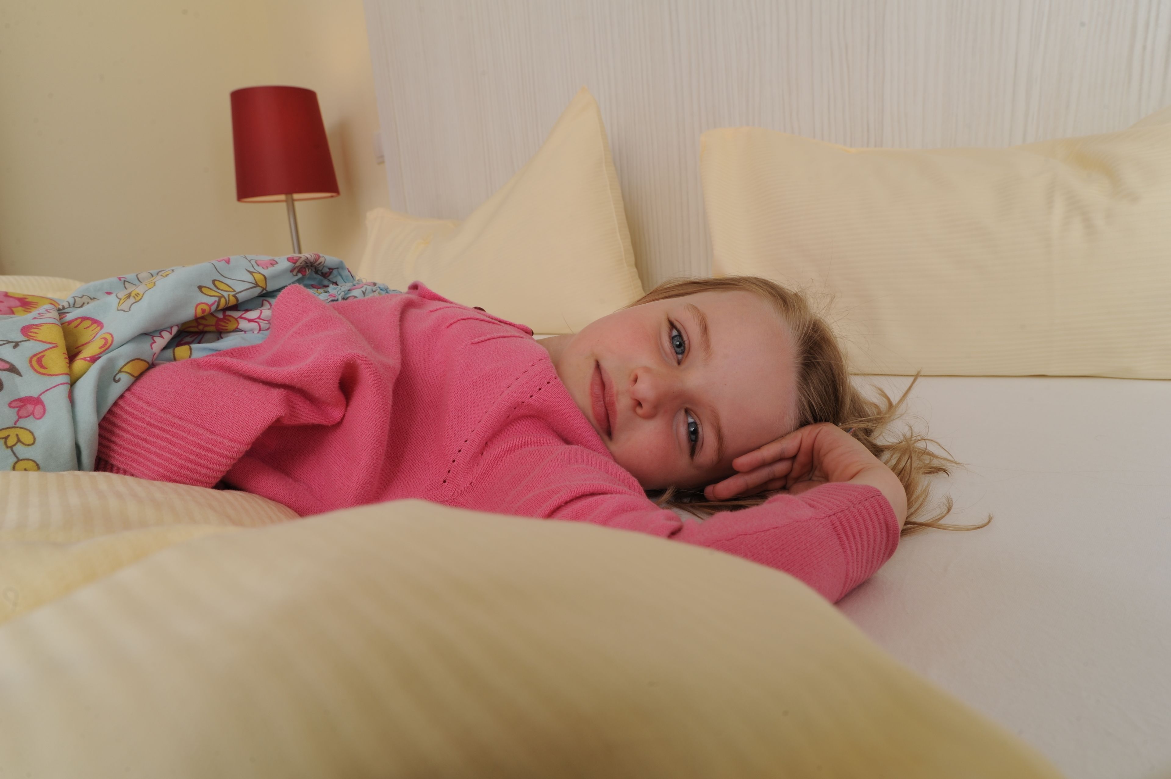 Ein Kind liegt auf einem Bett, im Hintergrund steht eine rote Lampe.