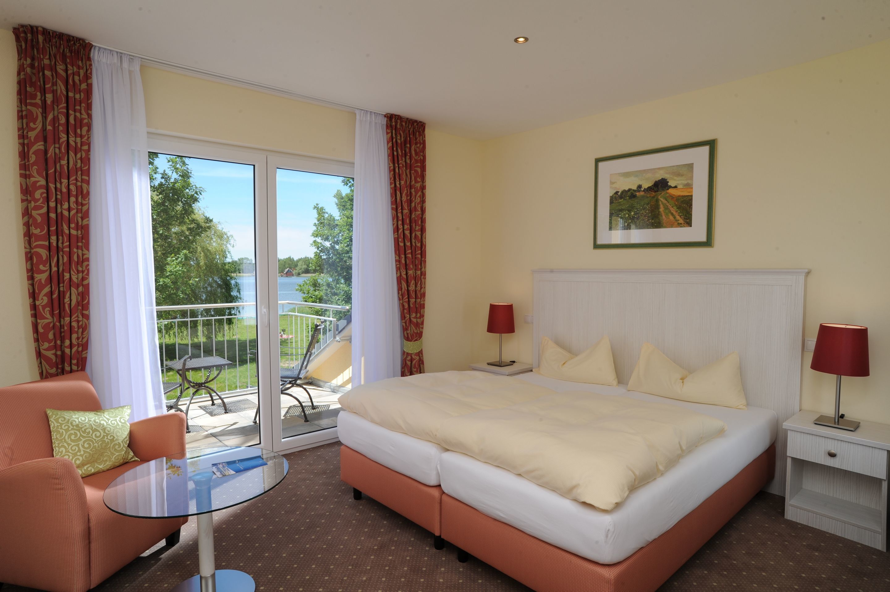 Habitación de hotel con cama, sofá, mesa y balcón con vistas a zonas verdes.