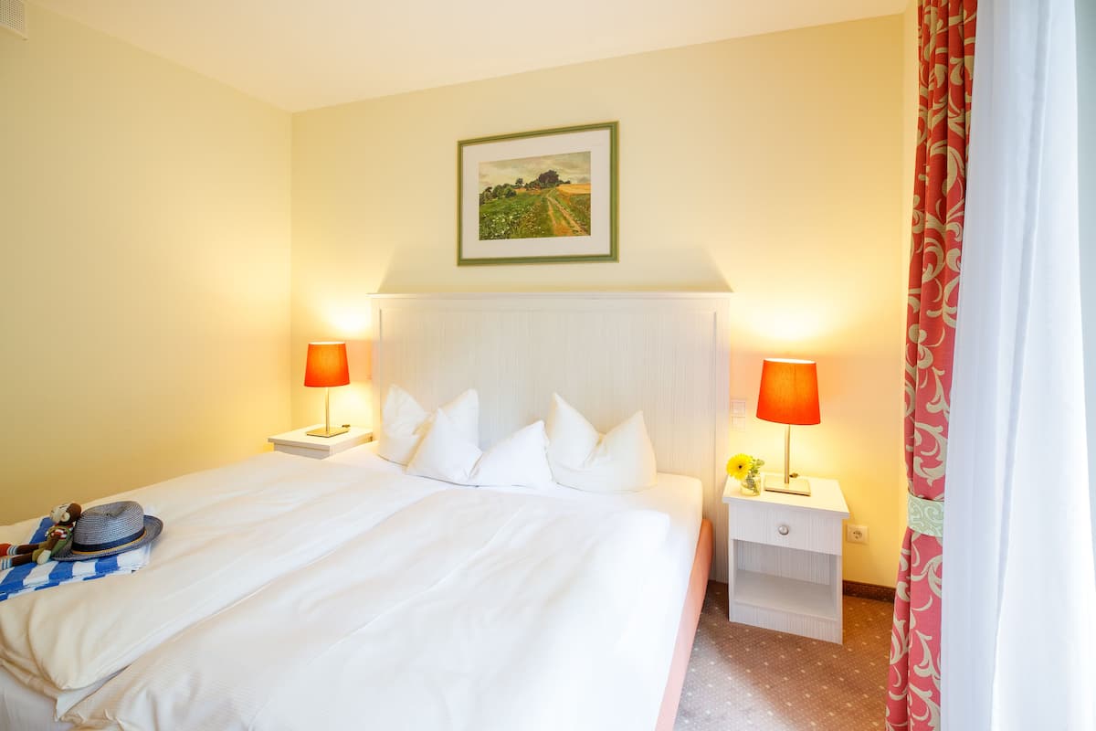 A hotel room with a large bed, two bedside tables, a nightstand, a framed picture on the wall, and a window with curtains.