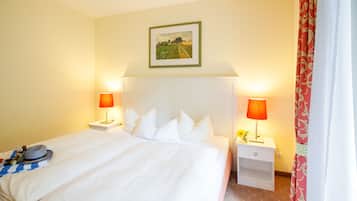 Quarto de hotel com uma cama grande, duas mesas de cabeceira, um criado-mudo, um quadro na parede e uma janela com cortinas.