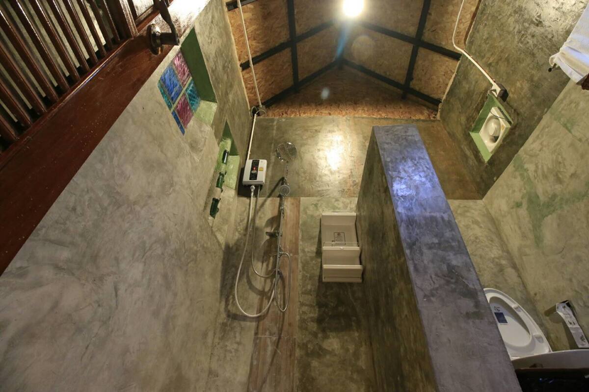 Een kleine, rustieke badkamer met houten vloer, een douche, toilet en wastafel.
