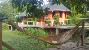 Un hamac sur une terrasse en bois, un pont et un bâtiment doté d’un toit incurvé.