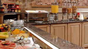 Un bufé de desayuno con diferentes opciones de comida, un dispensador de zumo y un mural decorativo de fondo.