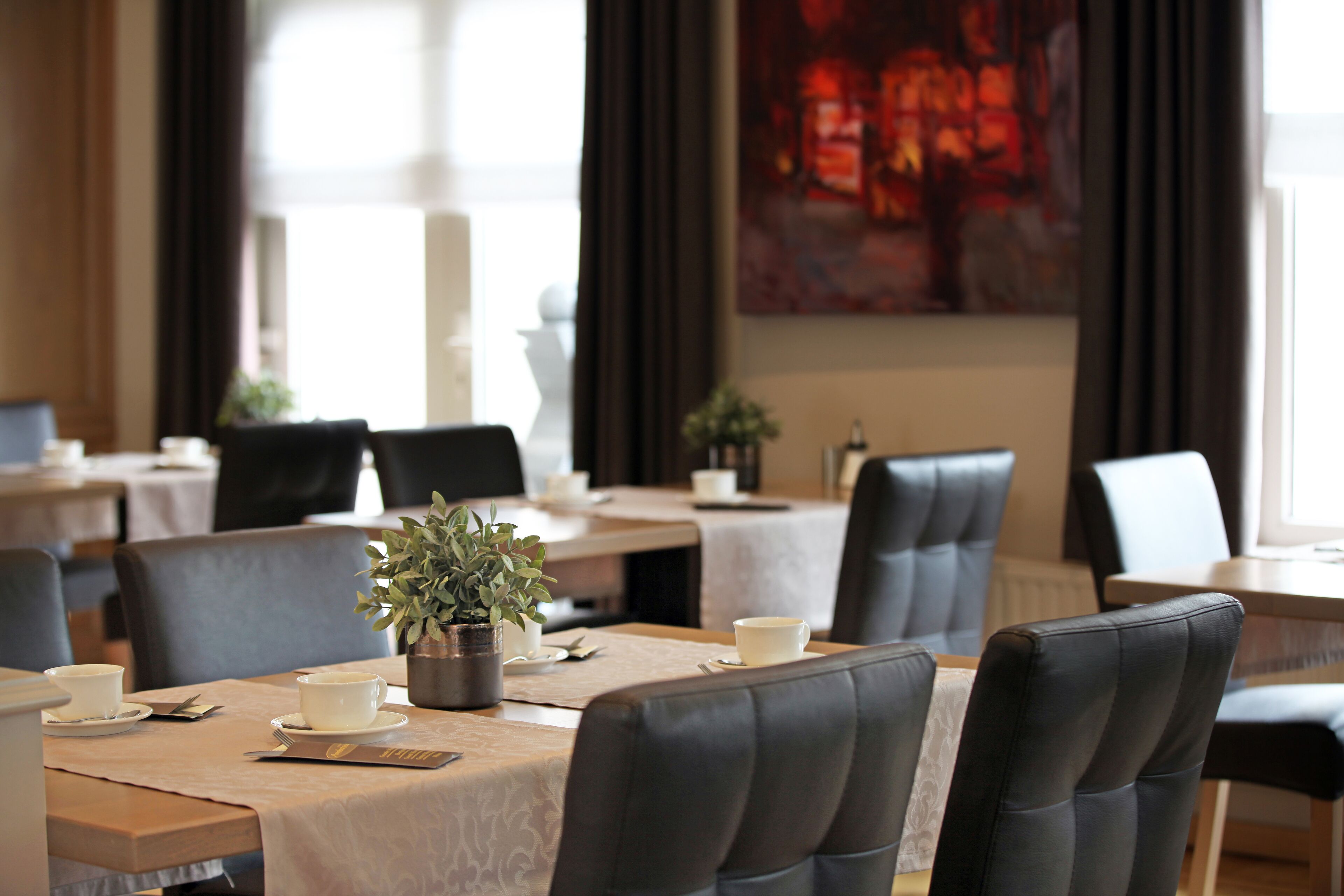 A dining area with tables set for four, each with a white tablecloth, black chairs, and a small potted plant.