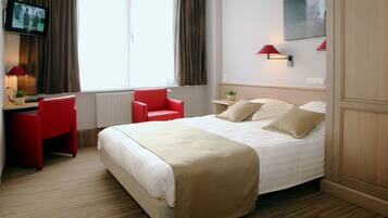 Een hotelkamer met een bed, een bureau met stoel, een televisie en een raam met gordijnen.