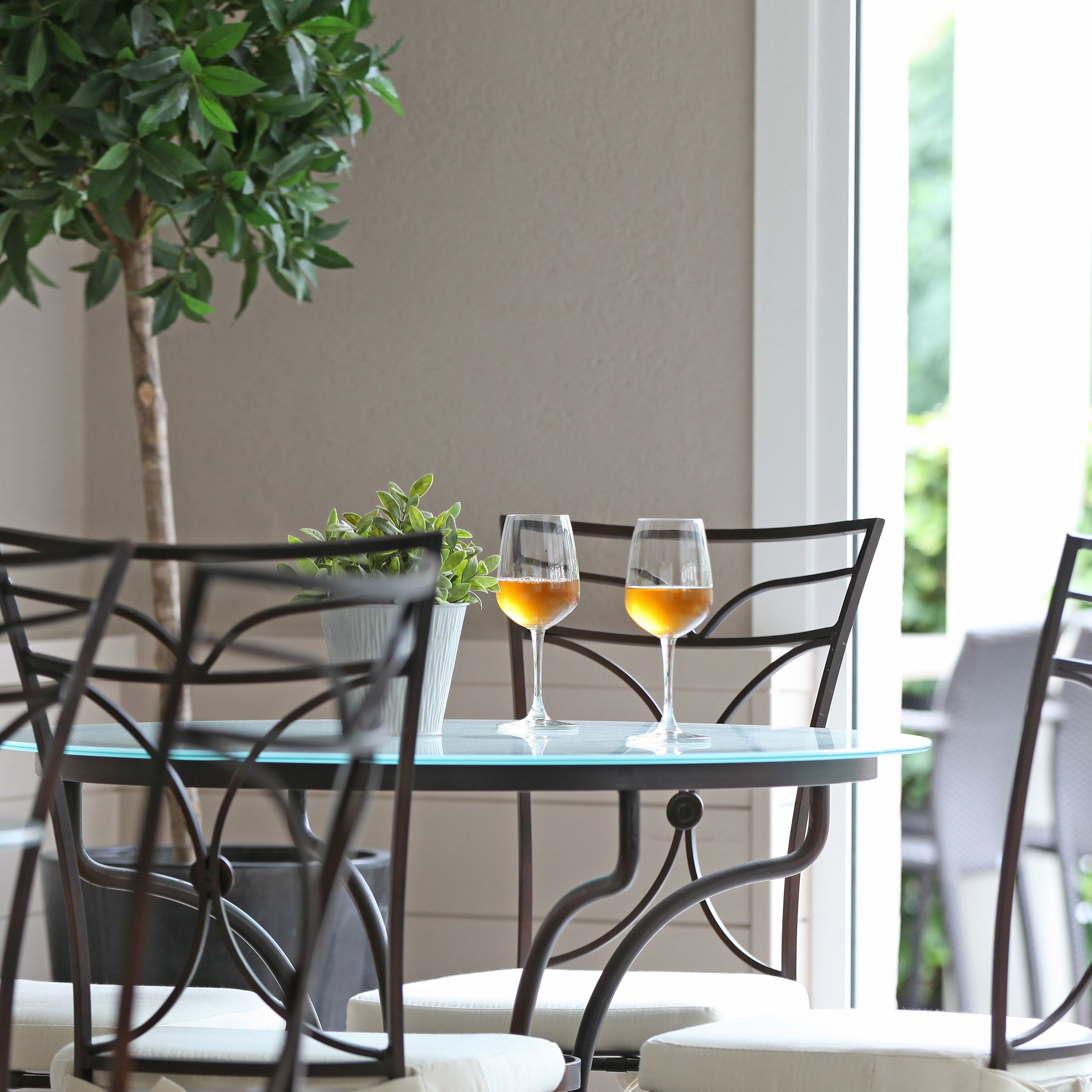 A glass table with two wine glasses, a potted plant, and a chair.