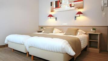 Ein Hotelzimmer mit zwei Betten, einem Spiegel an der Kopfteil, Wandlampen, einem Nachttisch mit Pflanze und einem kleinen Regal.