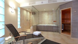 Un baño moderno con ducha envuelta en vidrio, una bañera amplia y una zona de estar con una mesa de vidrio y sillas.