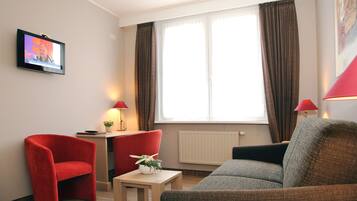 Una sala de estar moderna con un sillón rojo, un sofá gris, una mesita con una planta y un televisor en la pared.