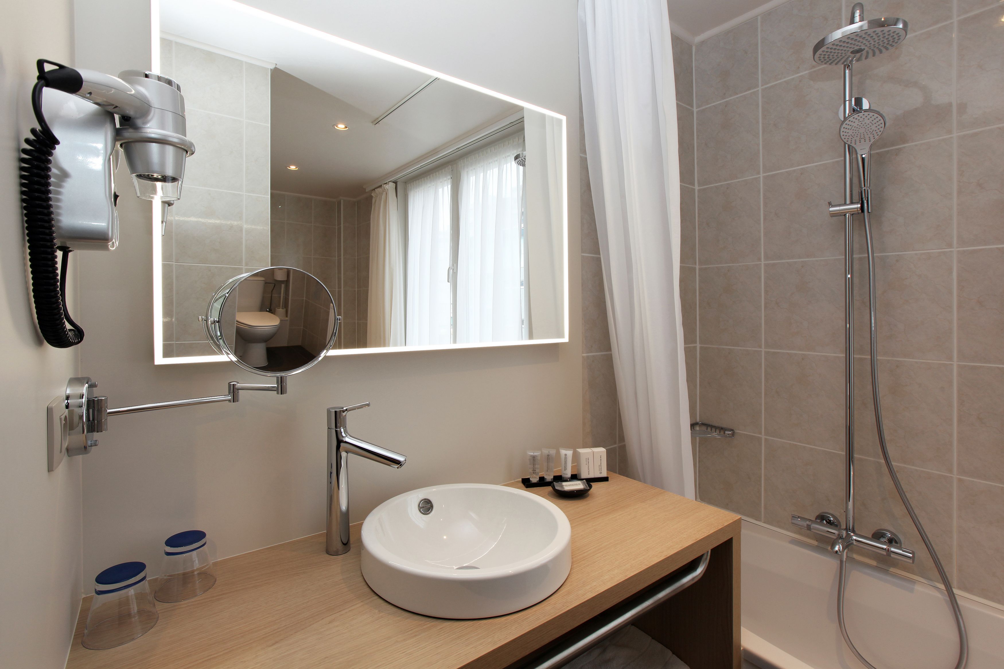 A modern bathroom with a round mirror, a sink, a hairdryer, and a shower.
