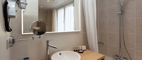 A modern bathroom with a round mirror, a sink, a hairdryer, and a shower.