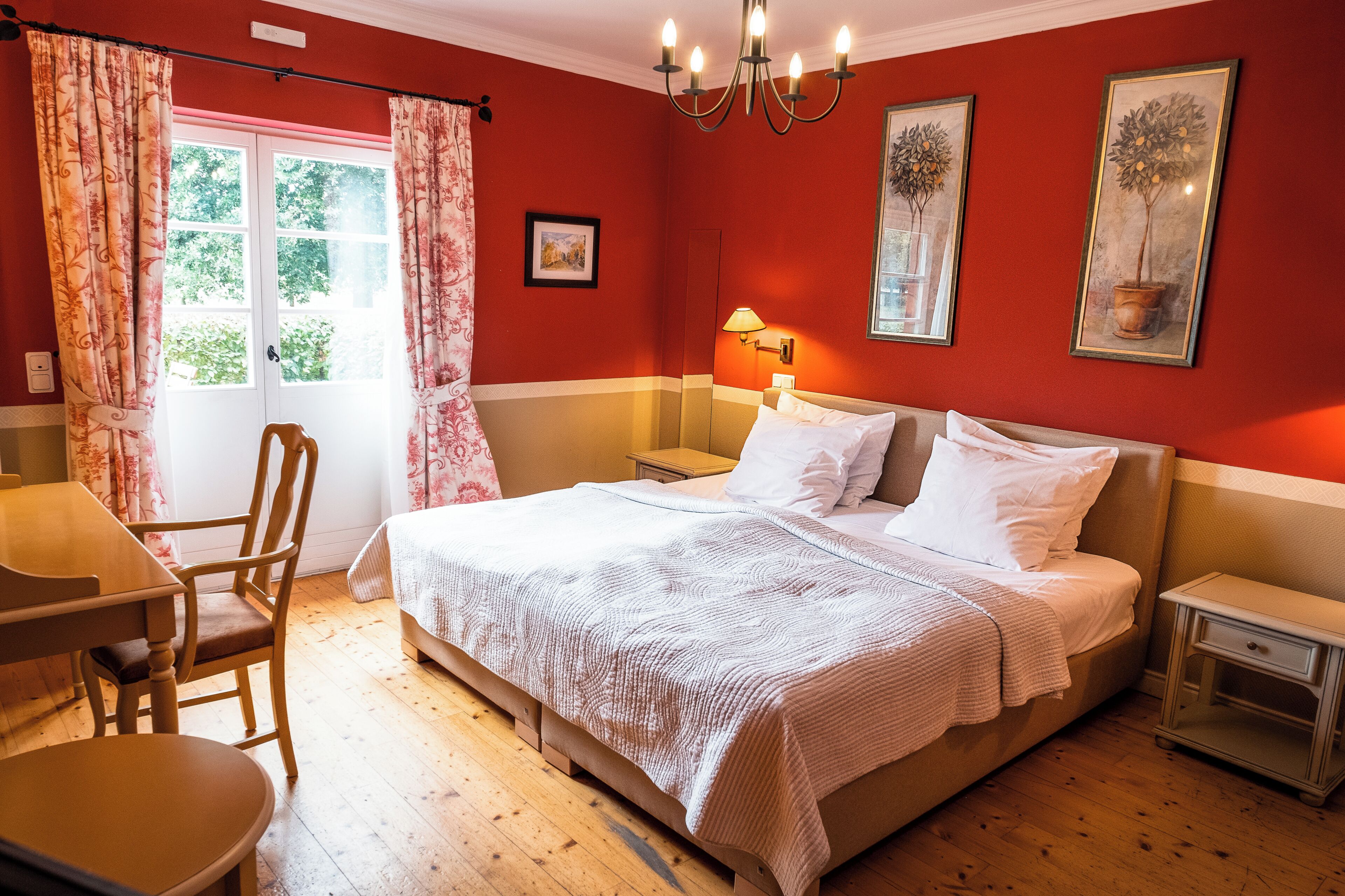 A bedroom with a bed, a desk, a chair, a nightstand, and a window with curtains.