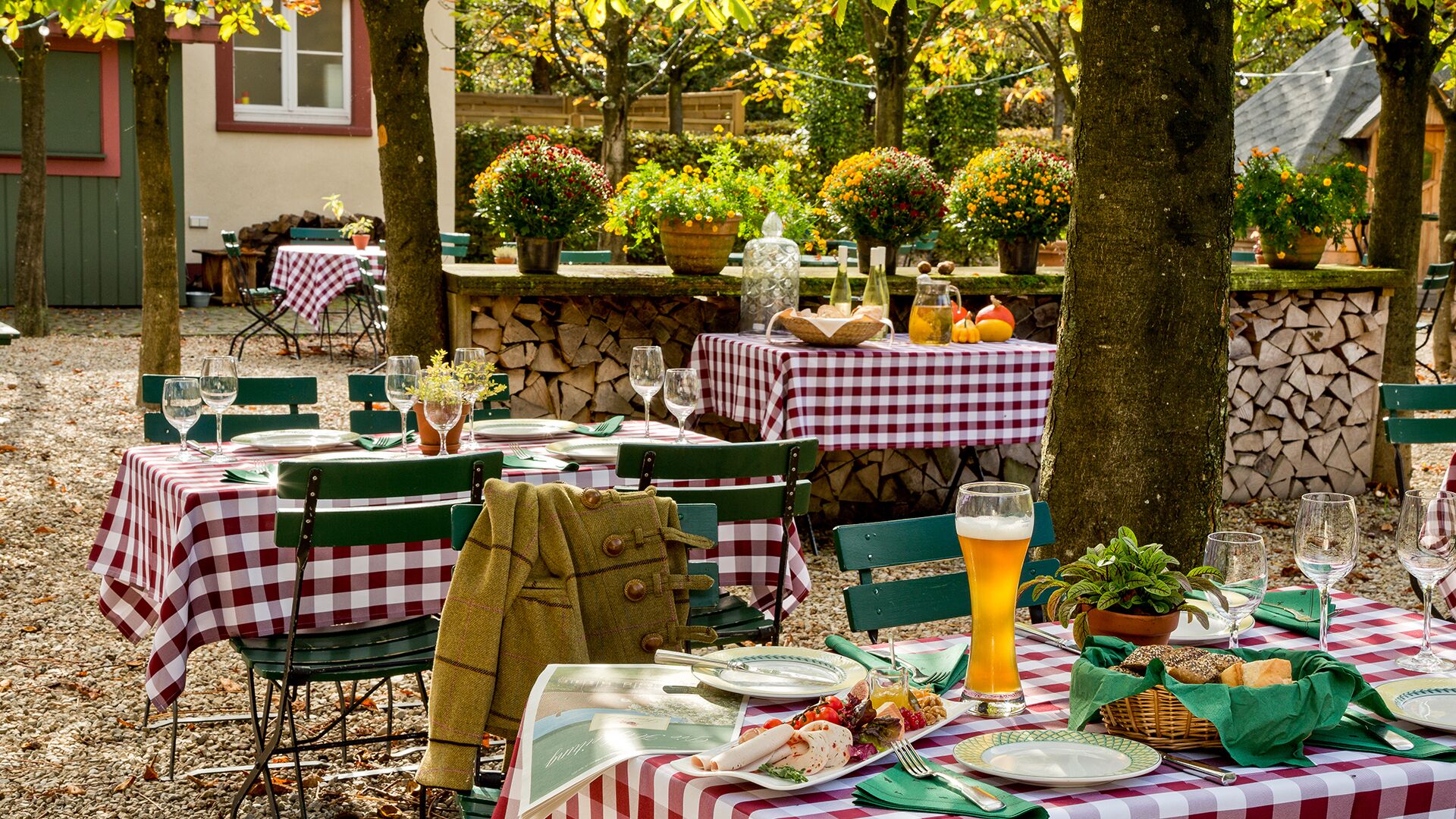 Un espace extérieur aménagé pour les repas, avec des tables recouvertes de nappes à carreaux, des chaises vertes et des plantes en pot.