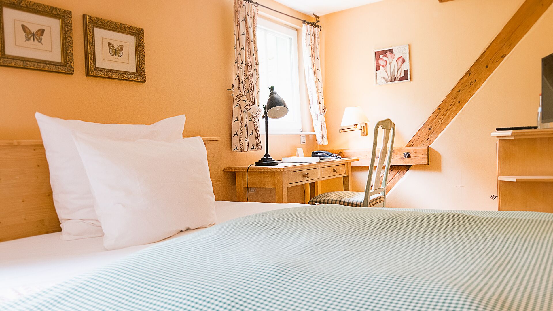 Ein Hotelzimmer mit Bett, Schreibtisch, Stuhl, Lampe und einem fensterbepflanzten Fenster.