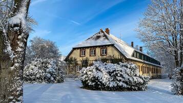 Una casa con techo inclinado, rodeada de árboles y arbustos cubiertos de nieve.