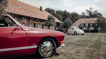 A red vintage car parked in front of a building with a tiled roof and a white vintage car in the background.