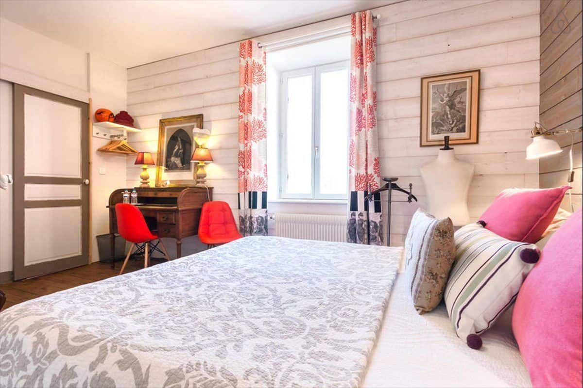 A bedroom with a bed, a desk, a chair, a radiator, and a window with curtains.