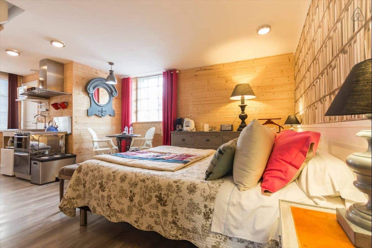 A cozy room with a bed, a desk, a chair, and a kitchenette.