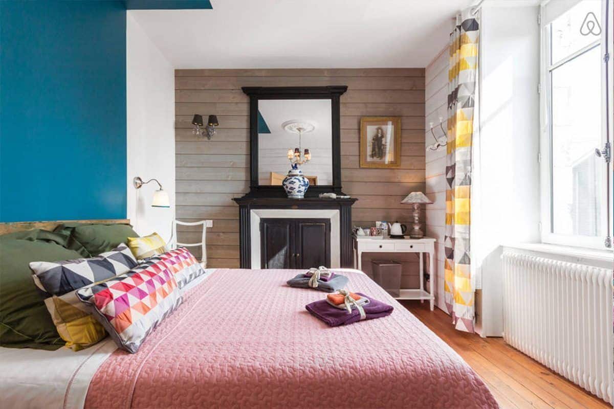 A bedroom with a bed, a dresser, a mirror, and a window with curtains.