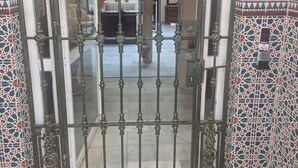 A wrought iron gate with a decorative top, leading to a room with patterned tile walls and a visible door. - Pensión Javier (Seville)
